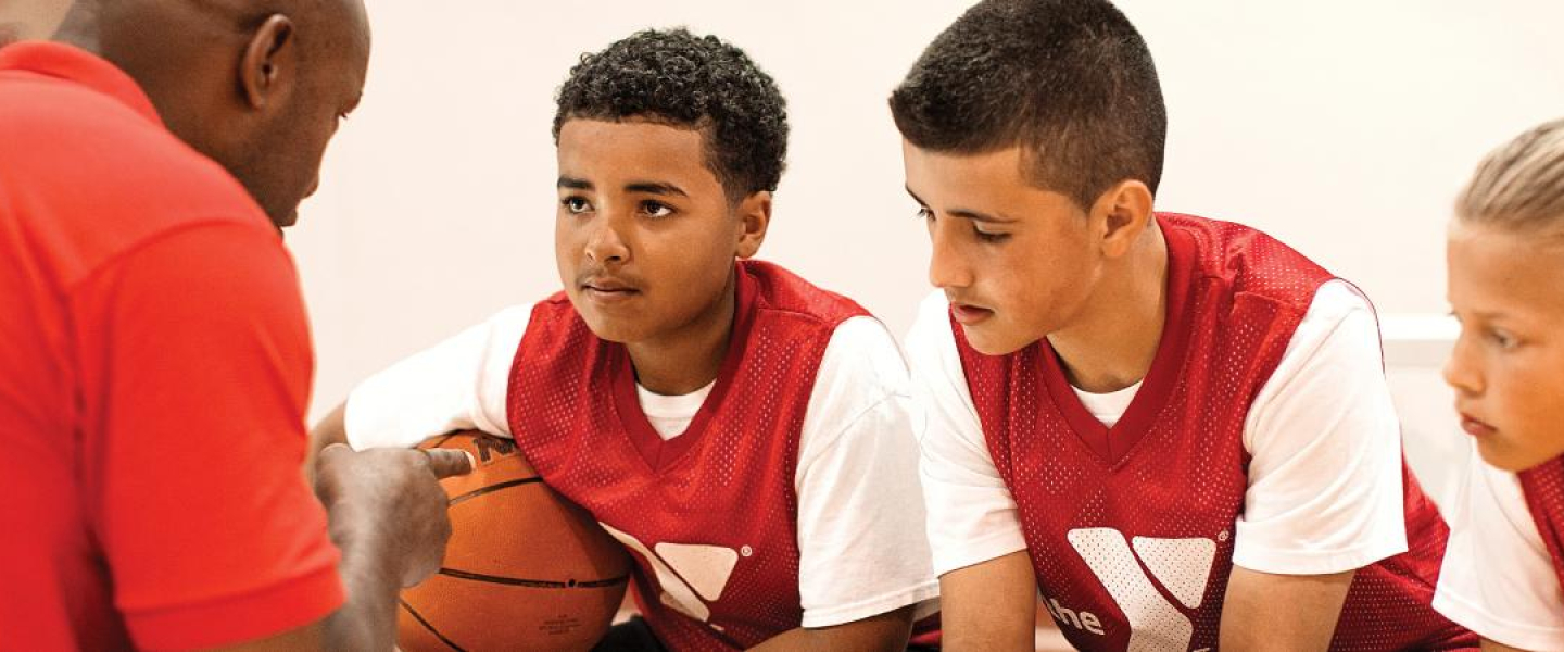 A coach instructing 3 youths in basketball.