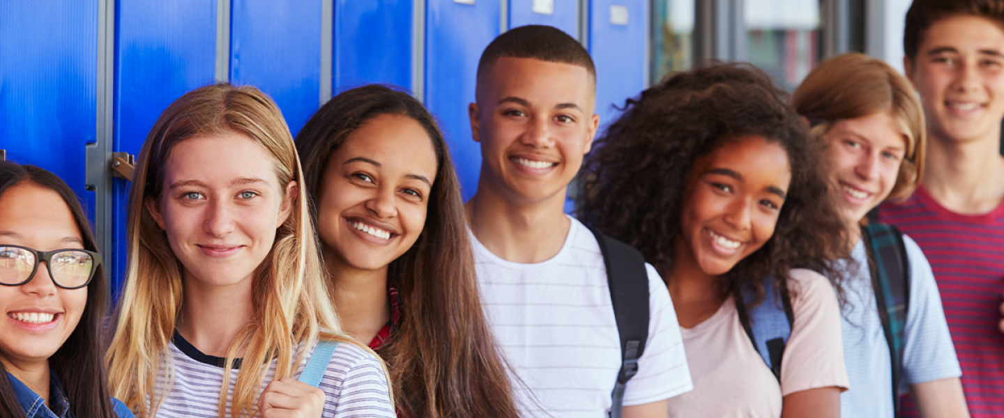 teens wearing backpacks smiling and standing in front of blue lockers