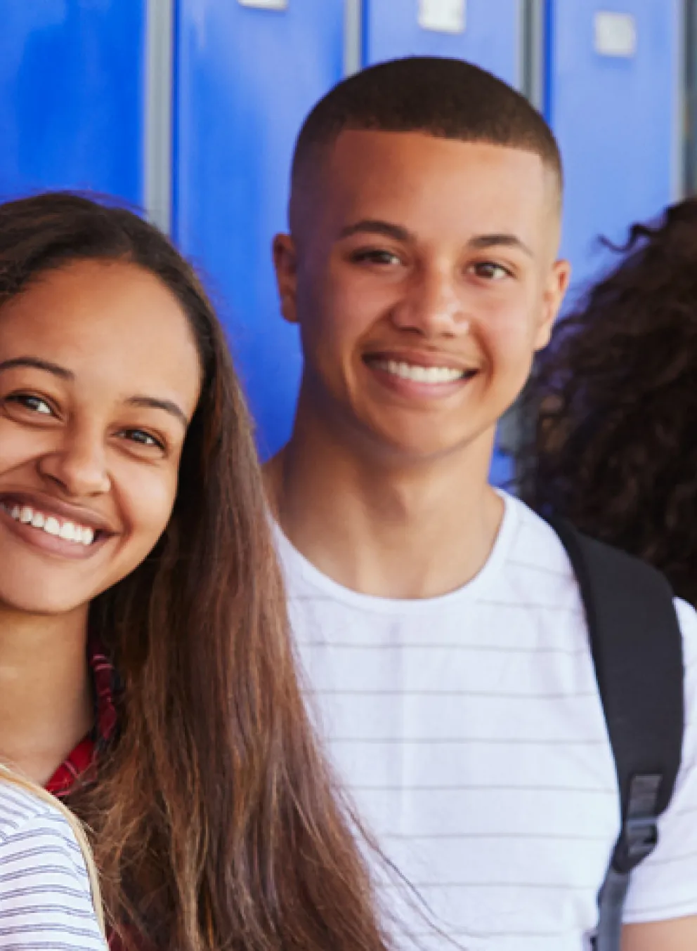 teens wearing backpacks smiling and standing in front of blue lockers