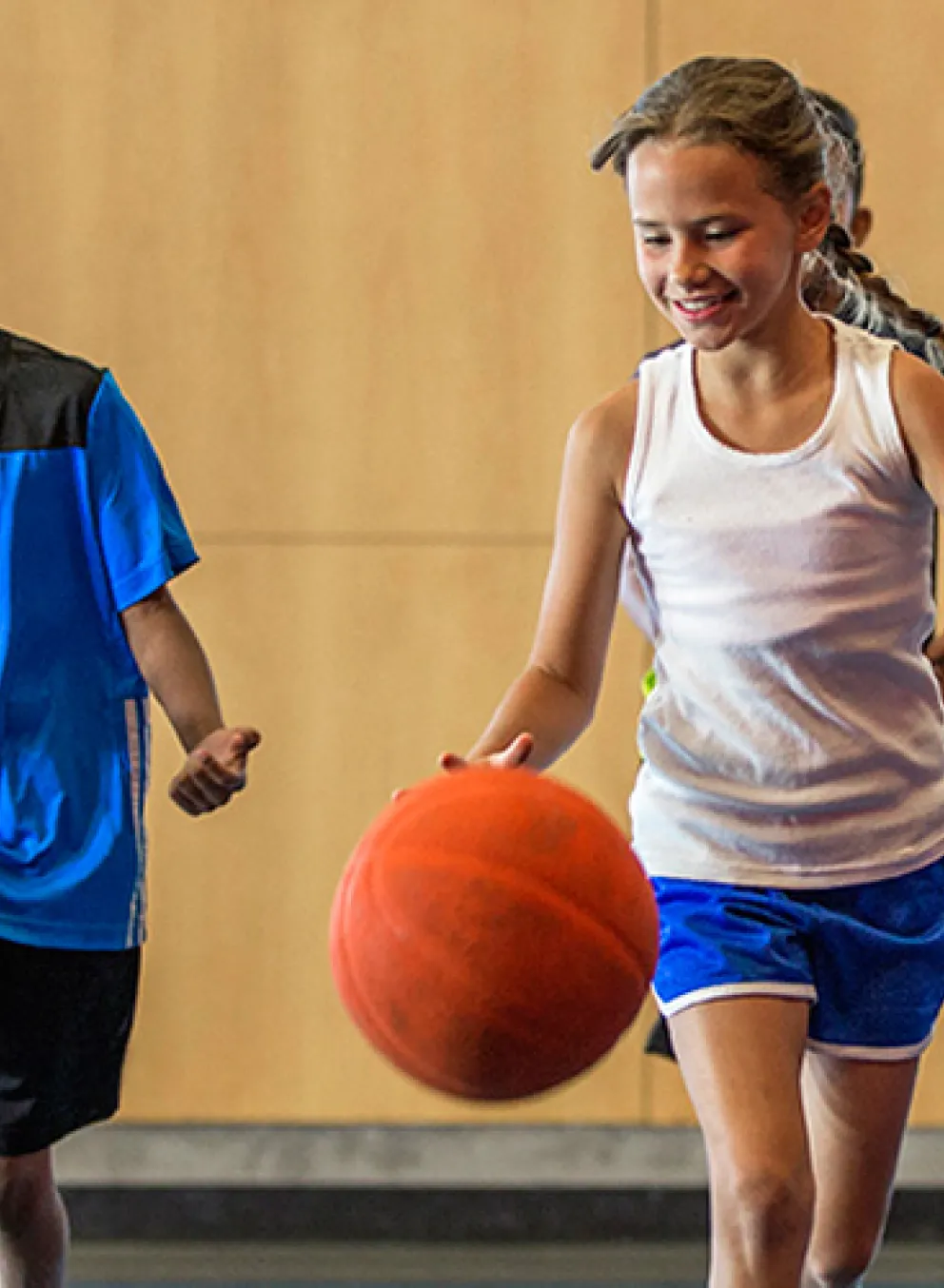 Four school age kids bouncing basketballs in indoor basketball gym.