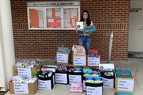 Aanya Patel from Global Girl's Initiative posing with boxes of donate female hygiene products