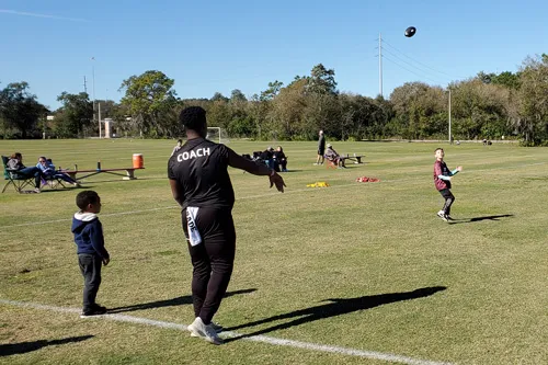coach and youth players practicing football in a large, open field