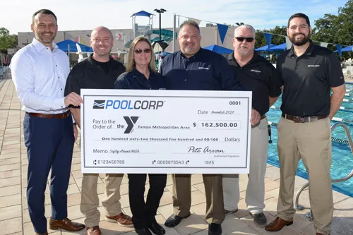 POOLCORP donation check presentation. Four men and one woman representing POOLCORP and Tampa Y CEO Matt Mitchell hold large check on the pool deck at the New Tampa Y. 